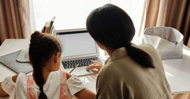 Majka i kći koji sjede za stolom na kojem se nalazi laptop