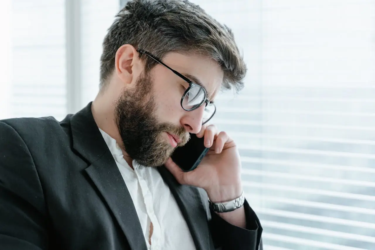 Muškarac u crnom sakou i bijeloj košulji razgovara na telefon